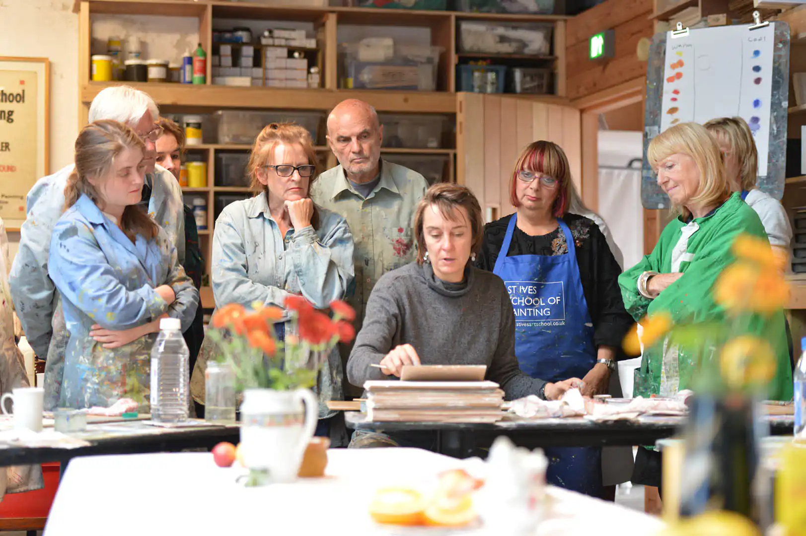 A diverse group of people gathered around a table at St Ives School of Painting, engaged in discussion and creativity.