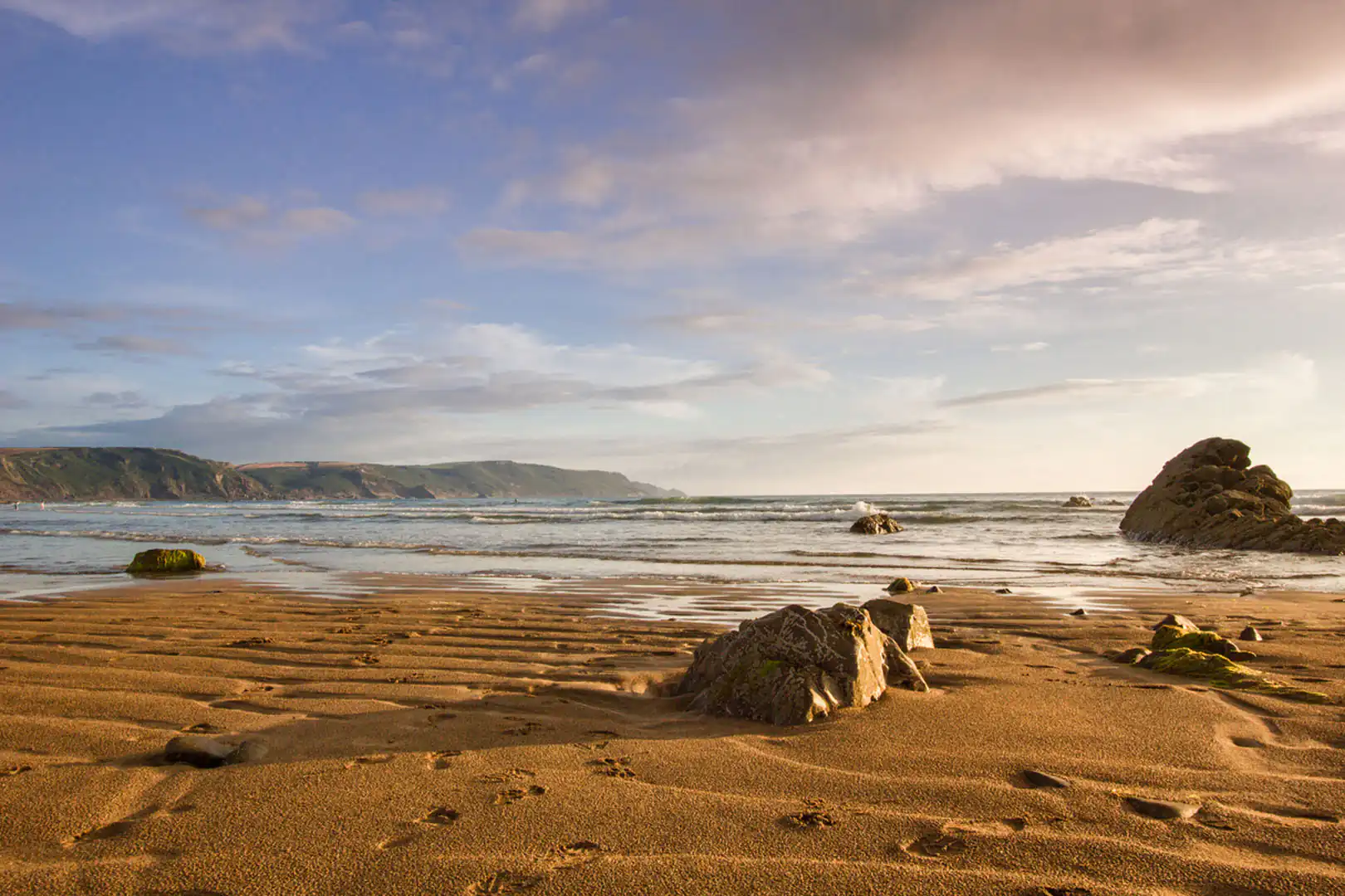 Scenic view of Widemouth Bay's sandy beach with rocks and water, ideal for exploring Cornwall's walking routes.