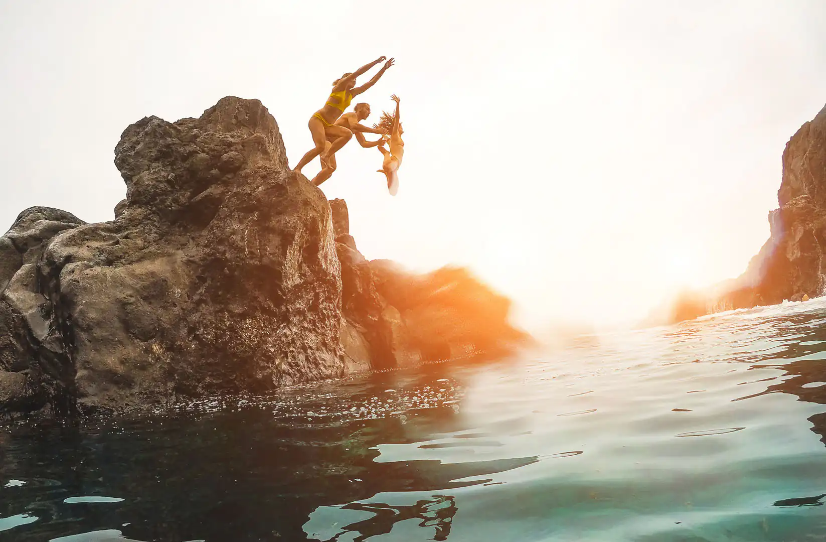A family joyfully jumps from a cliff into the sea, showcasing the thrill of adventure in Cornwall's beautiful coastline.