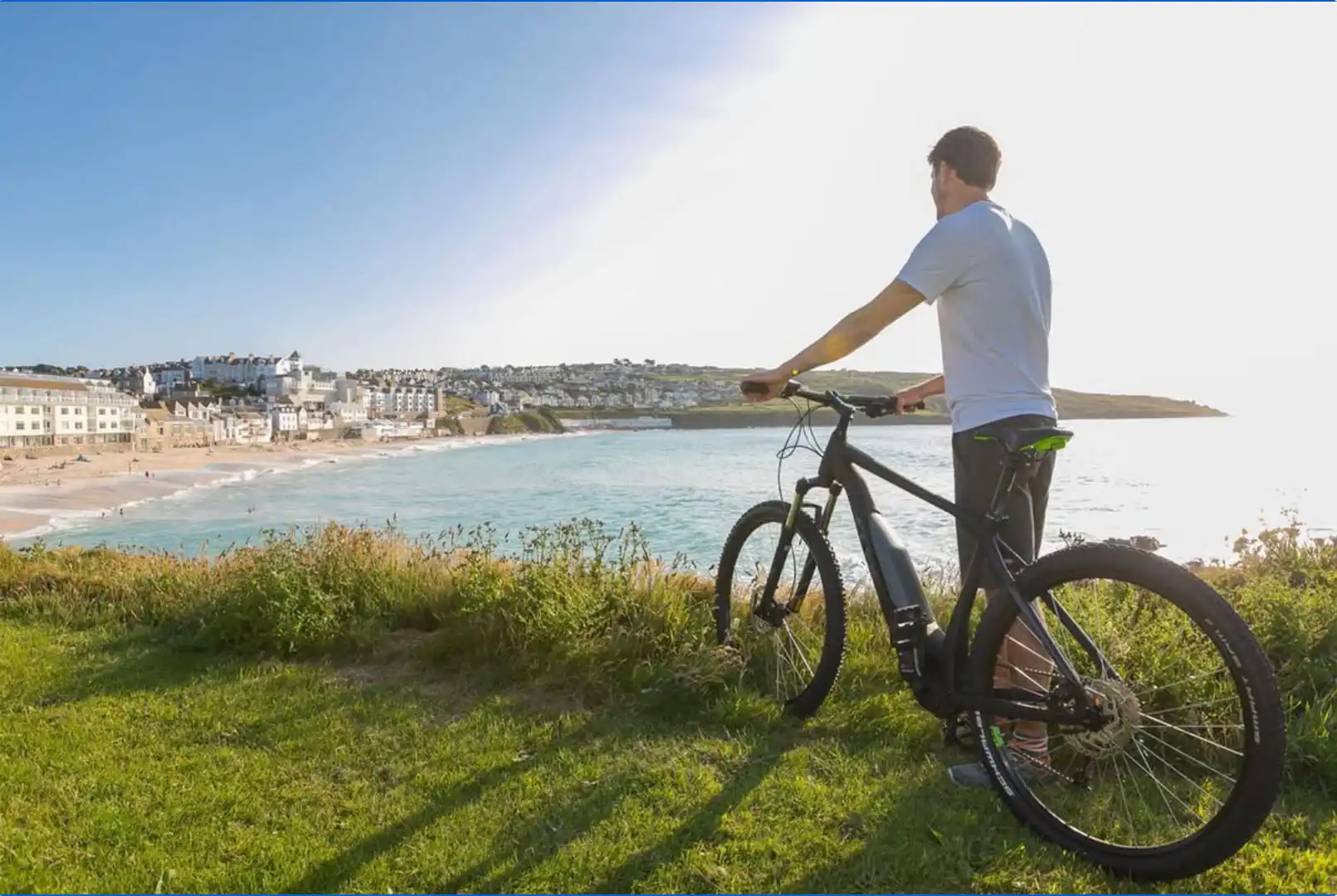 A man on a bike gazes at the ocean view from Porthmeor Beach in Cornwall, enjoying the scenic landscape, a great thing to do this September in Cornwall.