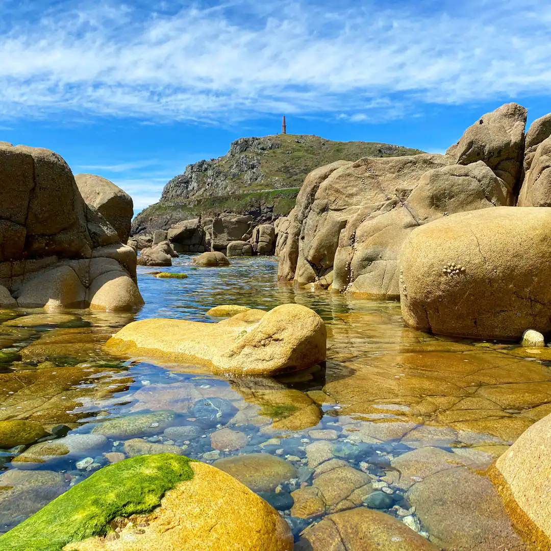 Rocky shoreline with water, a lighthouse in the background, and a rockpool, showcasing Cornwall's coastal beauty and a a great place for a guided walk with the Cornwall Geologist.