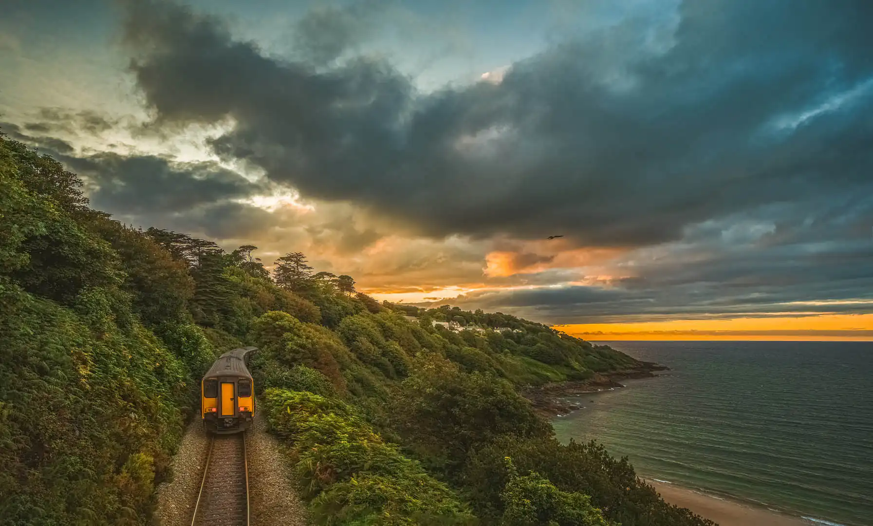 A train travels along the St Ives line, with the ocean shimmering beside the tracks in scenic Cornwall, the most scenic rail journey in Cornwall.